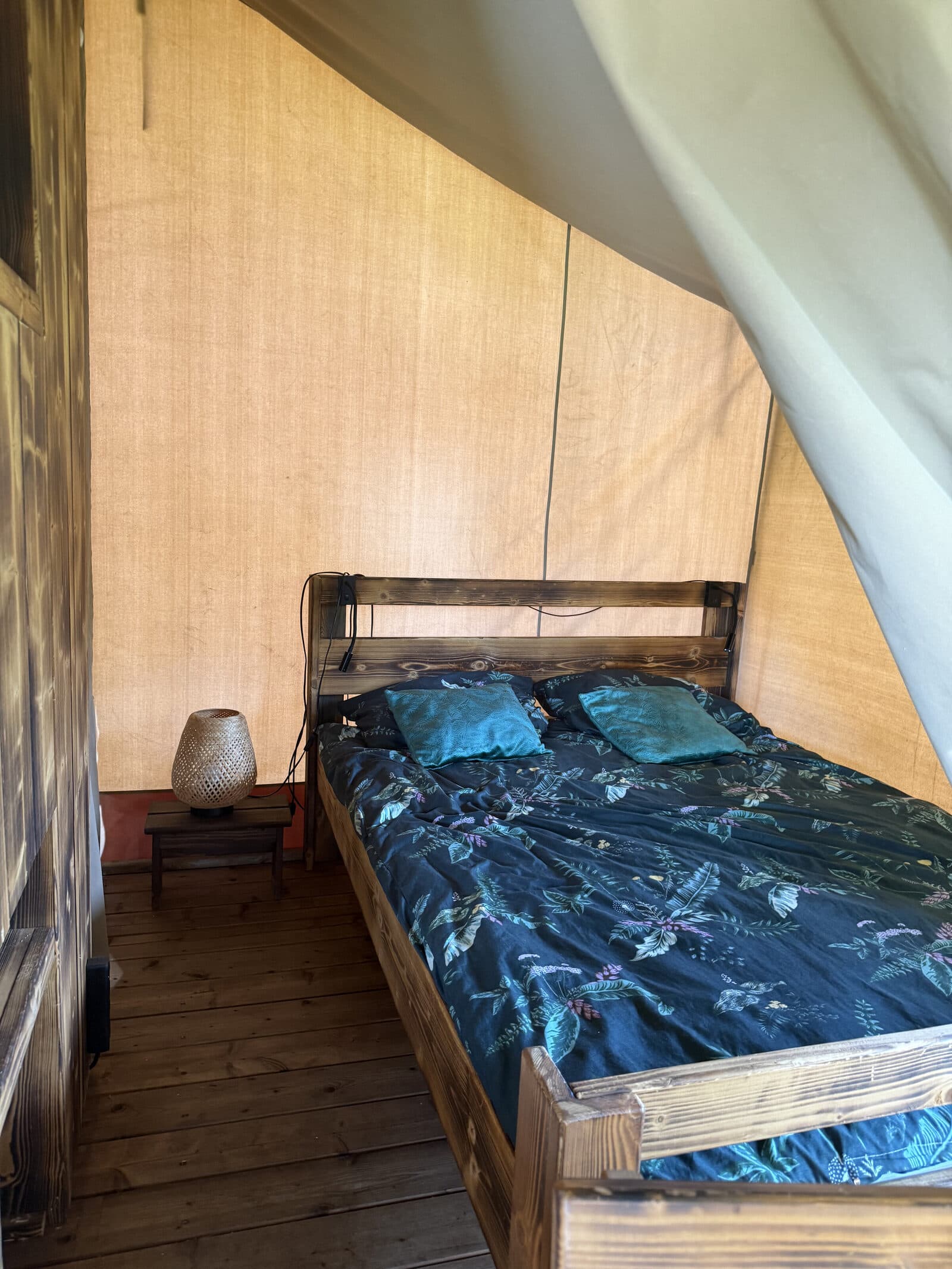 Wnętrze namiotu safari — łóżko z drewnianą ramą i pościelą